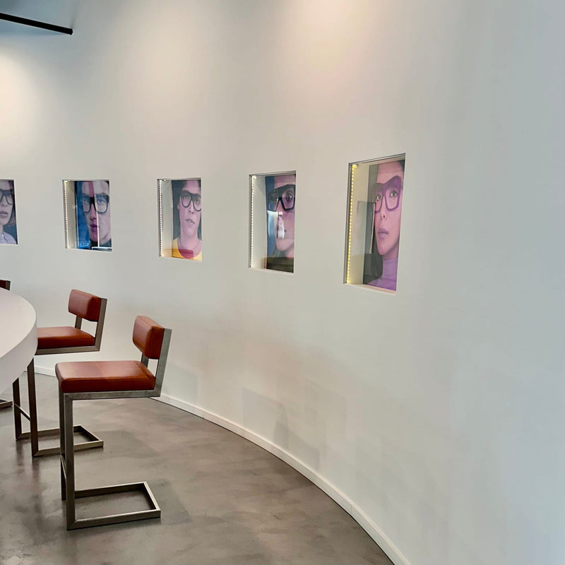Intérieur du magasin Bar à Lunettes avec des portraits encadrés et une variété de lunettes sur mesure disponibles pour les clients.